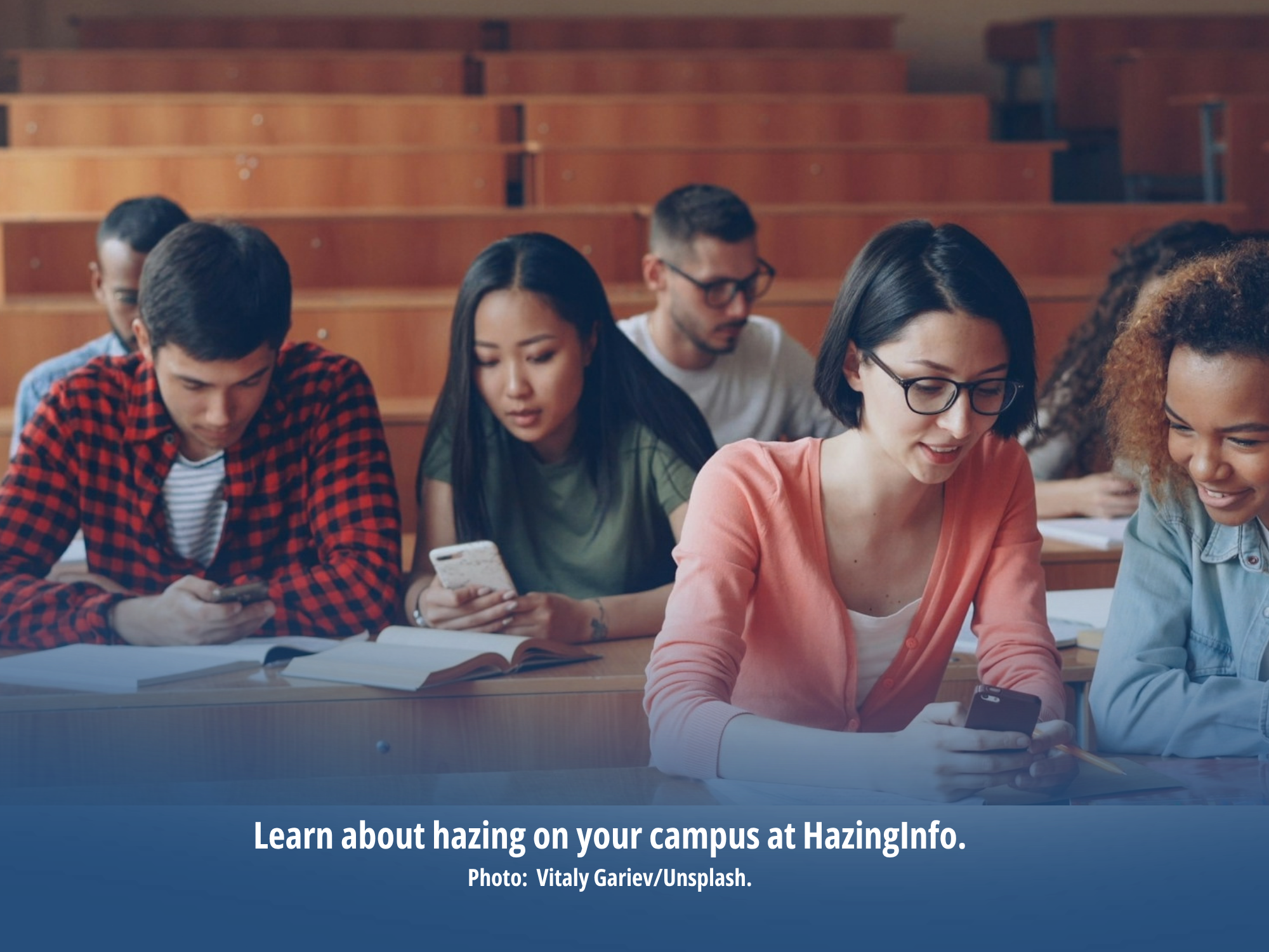 A diverse group of college students sits in a classroom, checking their cell phones.