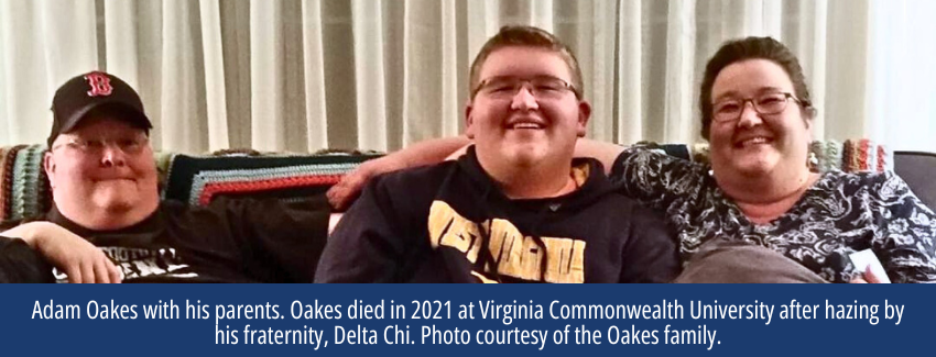 A young man with glasses sits on a couch between his father and mother.